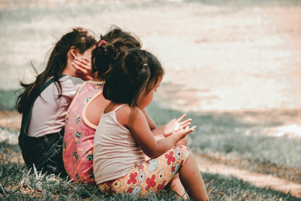 Three preschool children sitting in the grass together