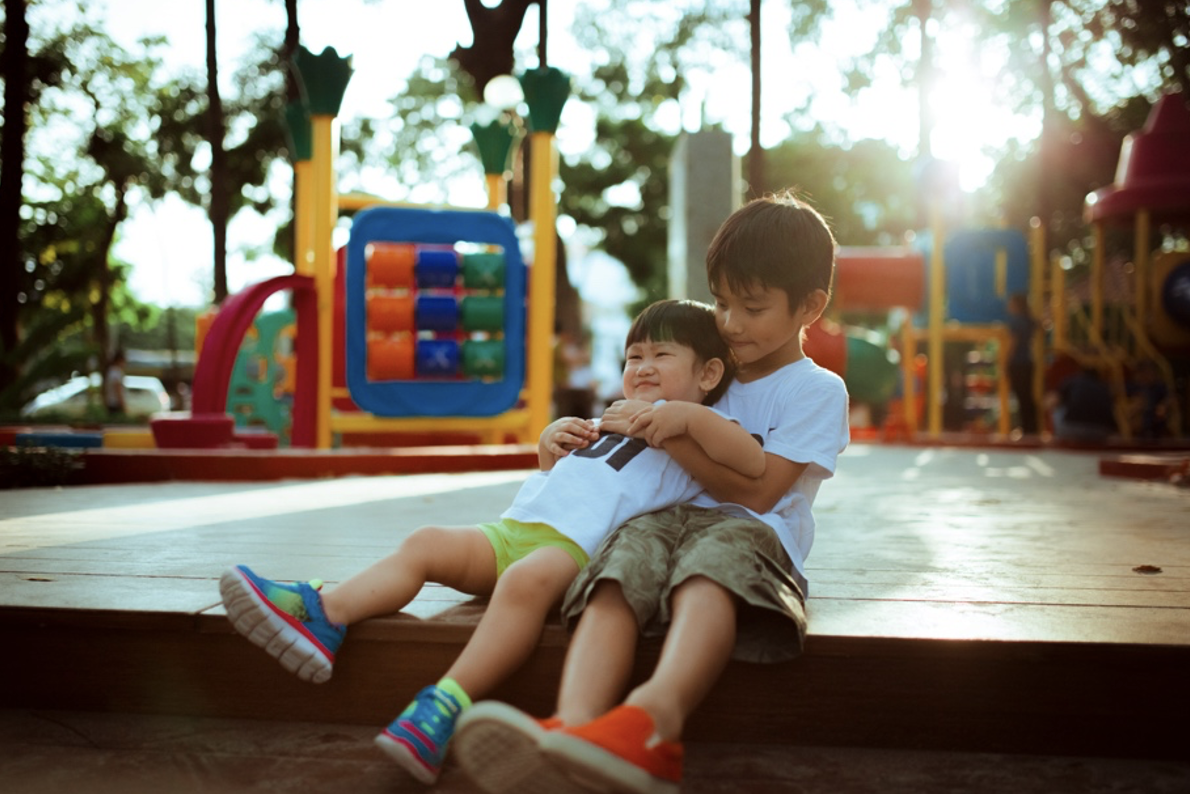 Two children playing together on the edge of a playground.